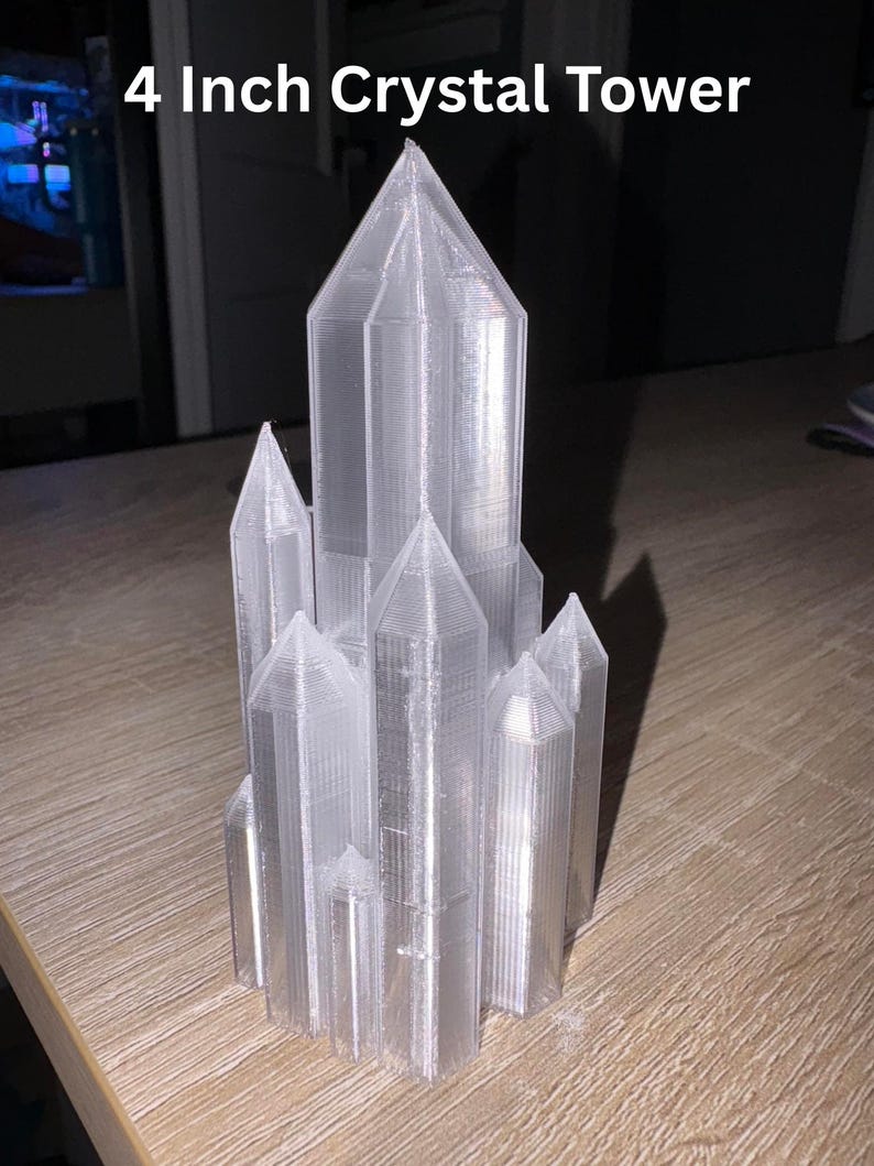 May include: A clear, 4-inch crystal tower with multiple spired structures. The text "4 Inch Crystal Tower" is displayed at the top. The tower is made of a translucent material and sits on a wooden surface.