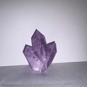K&ouml;nnte beinhalten: Ein Cluster aus lila Kristallformationen. Die Kristalle haben scharfe, spitze Kanten und eine strukturierte Oberfl&auml;che. Die Farbe ist ein leuchtendes, schimmerndes Lila, und die Gesamtform ist symmetrisch und ansprechend.