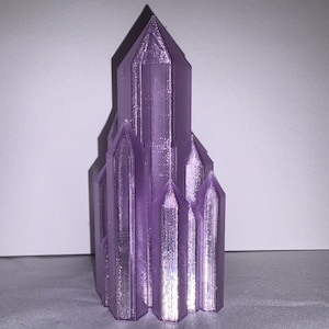 K&ouml;nnte beinhalten: Eine 3D-gedruckte, lila Kristallskulptur. Die Skulptur hat ein kathedralenartiges Design mit mehreren T&uuml;rmen und einer strukturierten Oberfl&auml;che. Die Farbe ist ein leuchtendes, metallisches Lila, und das Objekt steht vor einem neutralen Hintergrund.