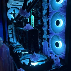K&ouml;nnte beinhalten: Ein individuell gestaltetes Computergeh&auml;use mit einem blau-wei&szlig;en Eisthema. Es verf&uuml;gt &uuml;ber blaue LED-L&uuml;fter, dekorative Eiskristallakzente und einen leuchtenden Innenraum. Die Gesamt&auml;sthetik ist ein cooler, futuristischer Look.