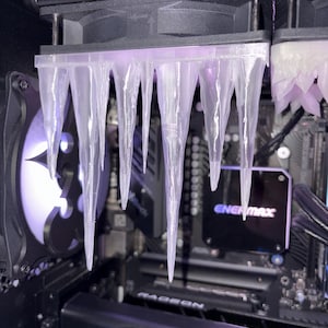May include: A computer's internal components, featuring a custom cooling setup. Transparent, icicle-like elements are suspended from above, bathed in a purple light. The system incorporates fans and a graphics card, with the "ENERMAX" logo visible.