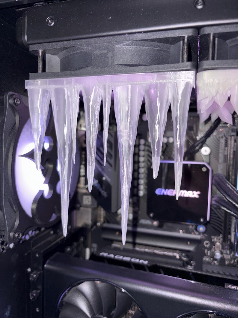 May include: A computer case interior with a custom cooling system. Clear, icicle-shaped components hang from the top, illuminated by a purple glow. The system includes fans and a graphics card, with the "ENERMAX" logo visible.