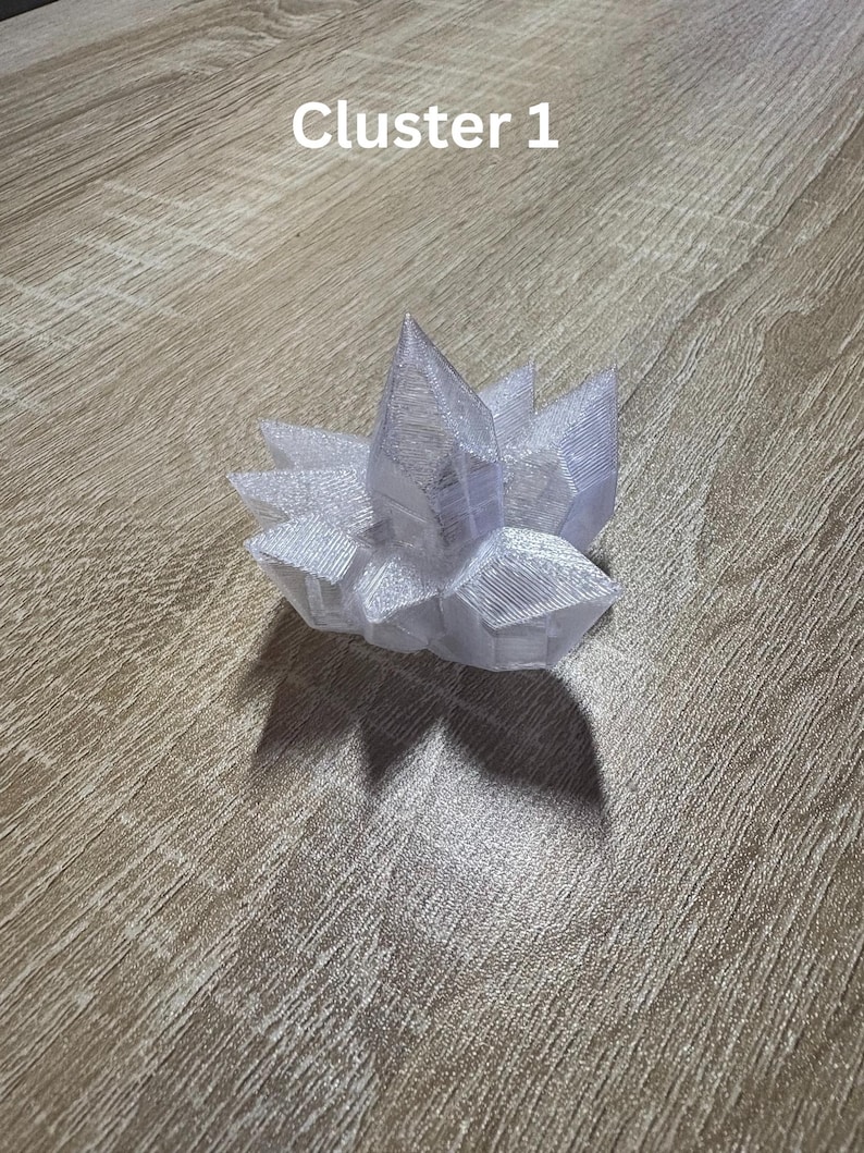 May include: A clear, crystalline cluster with a pointed top and multiple facets. The cluster is white and sits on a wooden surface. The text "Cluster 1" is visible in the upper left corner.