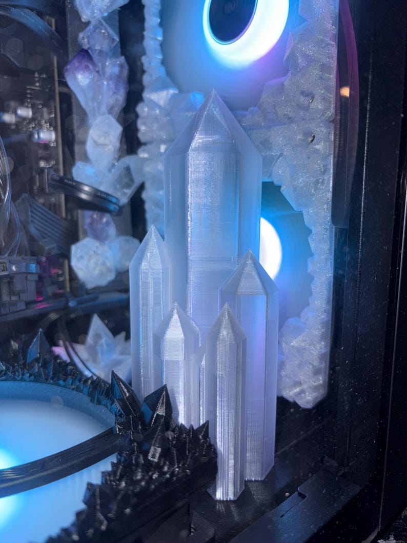 May include: A computer case interior featuring a cluster of clear, crystalline structures. The design includes a central arrangement of tall, pointed crystals, complemented by a dark, spiky accent piece. The scene is illuminated with blue and purple LED lighting.