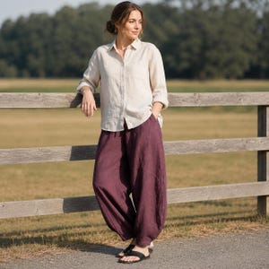 May include: A long-sleeved, button-down shirt in a light beige color paired with loose-fitting, wide-leg trousers in a deep plum purple shade. The shirt features a classic collar and a single chest pocket, while the trousers have a relaxed silhouette.
