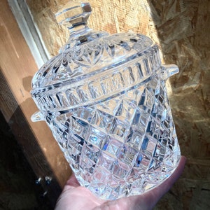 May include: A clear glass ice bucket with a lid, featuring a diamond-shaped pattern. The bucket has two handles on the sides.