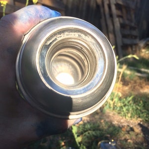 May include: Close-up view of the inside of a silver thermos bottle. The opening of the bottle is round and has a shiny, metallic finish.