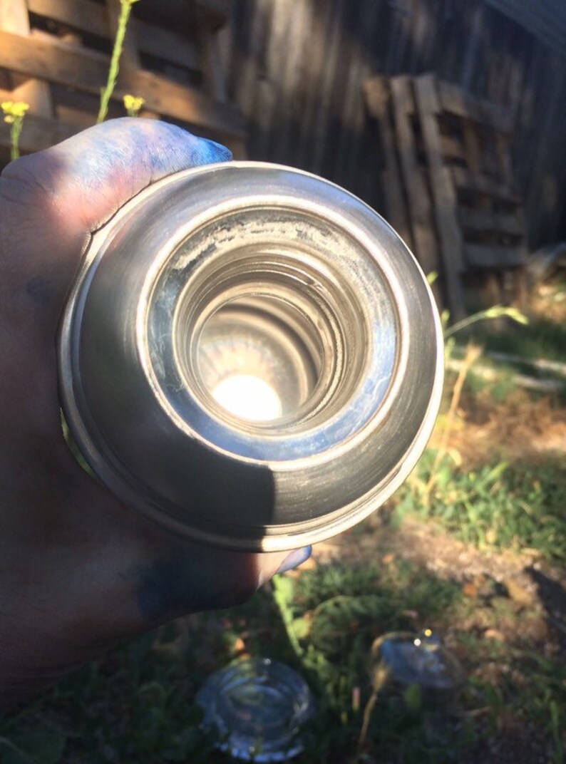 May include: Close-up view of the inside of a silver thermos bottle. The opening of the bottle is round and has a shiny, metallic finish.