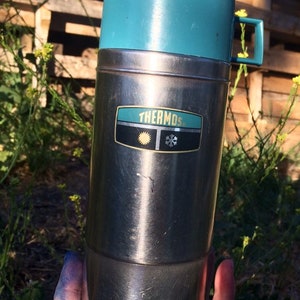 May include: A silver thermos with a teal blue lid and a black and yellow "THERMOS" logo with a sun and snowflake.