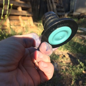 May include: A black plastic bottle stopper with a teal rubber seal. The stopper has the text "TIGHTEN" printed on it.