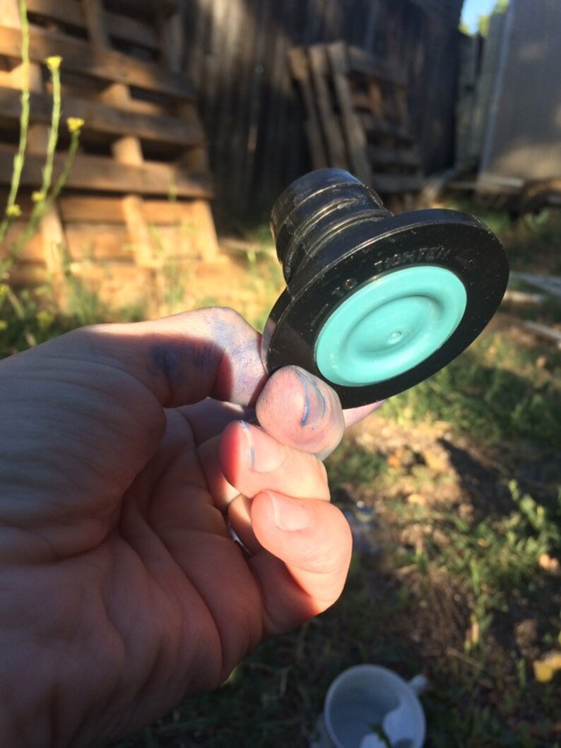 May include: A black plastic bottle stopper with a teal rubber seal. The stopper has the text "TIGHTEN" printed on it.