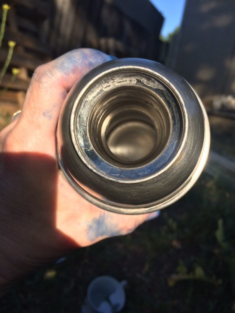 May include: Close-up of the inside of a silver thermos with a shiny, reflective surface.