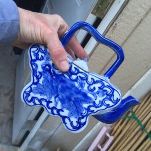 May include: A blue and white porcelain teapot with a floral design. The teapot has a handle and a spout. The teapot is decorated with blue flowers and leaves on a white background.