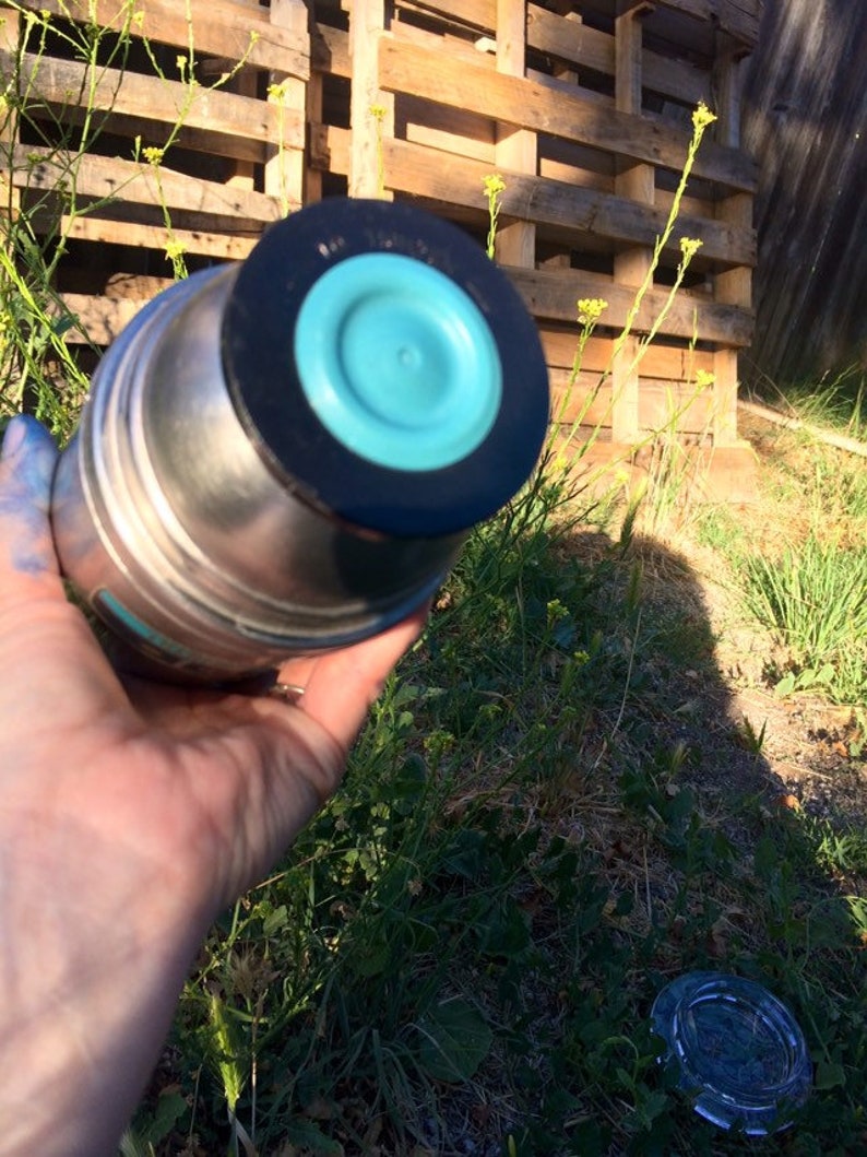 May include: A stainless steel water bottle with a turquoise blue lid and a black rubber ring. The bottle is sitting on a wooden pallet.