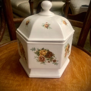 May include: White ceramic octagonal canister with a lid and floral design. The canister has a white background with brown, yellow, and green floral accents.
