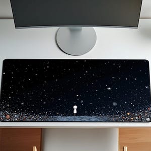 May include: A black rectangular desk mat with a starry night design, featuring a small figure. The mat is on a white desk with a computer monitor, a silver desk lamp, and a wooden chair. Plants are in the background.