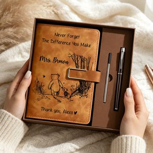 Op de afbeelding: Een beige notitieboek in lederlook in een geschenkdoos met een zwarte pen en vulling. De kaft bevat een Winnie de Poeh-illustratie, een metalen sluiting en de tekst: Never Forget The Difference You Make, Mrs. Brown, Thank you, Alexs met een hartje.