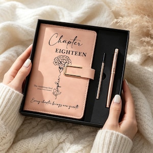 May include: A peach-colored journal with a gold-tone metal clasp, featuring the text Chapter EIGHTEEN, a carnation illustration, the name Sophia, and the phrase Every chapter brings new growth, presented in a black gift box with a matching pen.