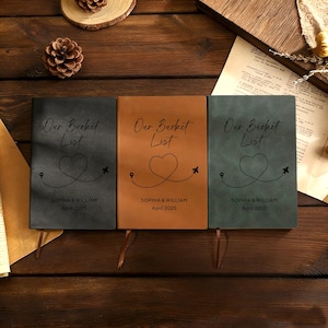 May include: Three personalized notebooks with the text "Our Bucket List" and the names "Sophia & William" with the date "April 2025". The notebooks are in black, brown, and green, with a heart and airplane design.