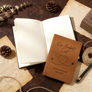 May include: A brown leather-bound journal with the words "Our Bucket List" and a heart-shaped travel route design. The journal is open next to a blank notebook. The cover also includes the names "Sophia & William" and the date "April 2025".