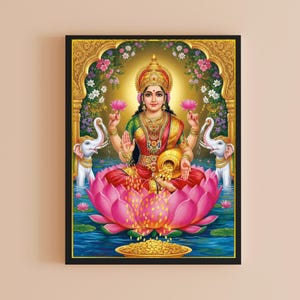 May include: A framed print of the Hindu goddess Lakshmi, seated on a pink lotus flower. She wears a red sari, gold jewelry, and a crown. Two white elephants flank her, and a golden pot overflows with coins. The background features a golden archway and floral accents.
