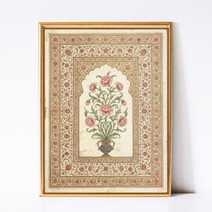 May include: A framed floral print with a gold border. The artwork features a central vase with pink flowers and green leaves. The background is a cream colour with a decorative border of red and gold floral patterns. The frame is a warm gold colour.