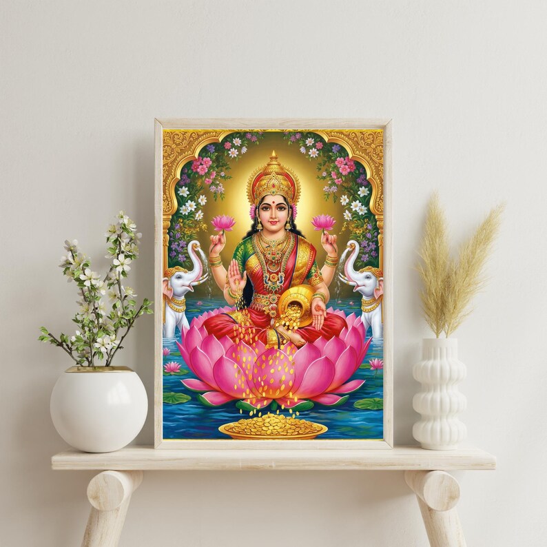 May include: A framed print of Lakshmi, the Hindu goddess of wealth, prosperity, and beauty. She is depicted seated on a pink lotus flower, holding lotus flowers and a pot of gold. The artwork features vibrant colors and intricate details, with floral and elephant motifs.