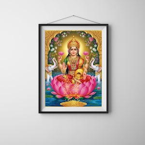 May include: Framed print of Lakshmi, the Hindu goddess of wealth, prosperity, and beauty. She is depicted seated on a large pink lotus flower, holding lotus flowers in two hands. Two white elephants flank her, and a golden arch frames the scene.