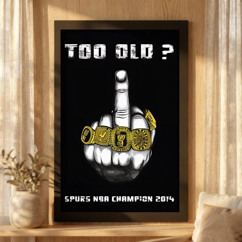 May include: A framed black and white poster featuring a hand with a raised middle finger wearing four gold championship rings. The text "TOO OLD ?" appears at the top, and "SPURS NBA CHAMPION 2014" is printed in white at the bottom of the print.