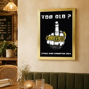 May include: A framed rectangular wall art piece featuring a black background with a white illustration of a hand making a middle finger gesture. The fingers are adorned with gold championship rings. Text reads TOO OLD? and SPURS NBA CHAMPION 2014.