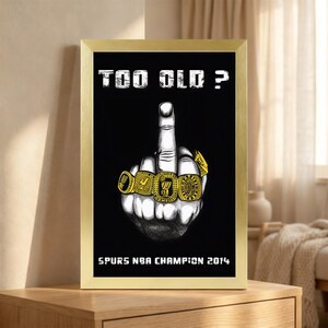 May include: A framed poster featuring a black background with the white text "TOO OLD ?" at the top and "SPURS NBA CHAMPION 2014" at the bottom. In the center is a black and white illustration of a hand showing the middle finger wearing four gold rings.