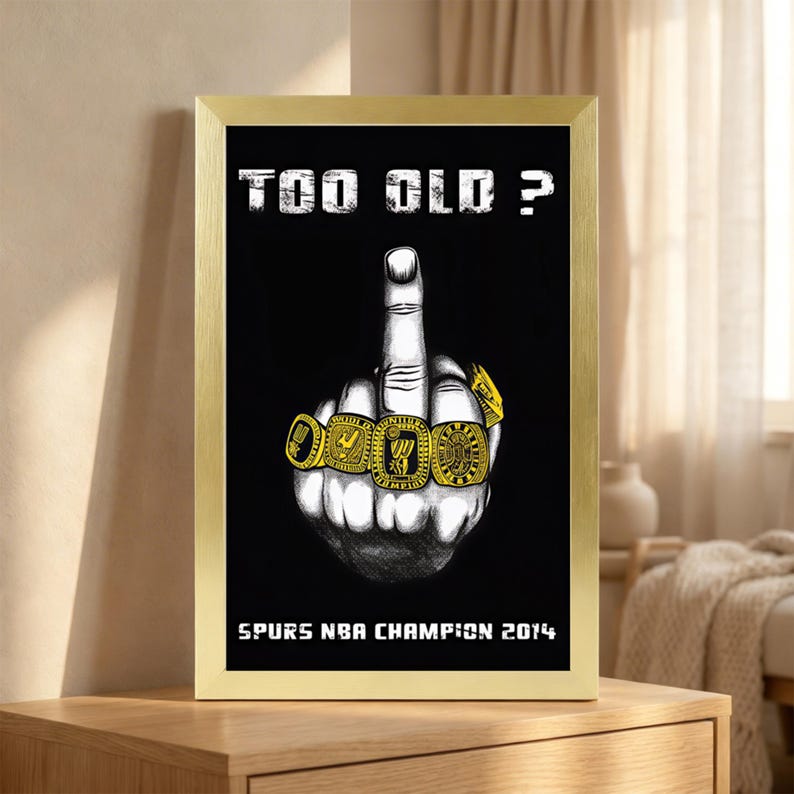 May include: A framed poster featuring a black background with the white text "TOO OLD ?" at the top and "SPURS NBA CHAMPION 2014" at the bottom. In the center is a black and white illustration of a hand showing the middle finger wearing four gold rings.