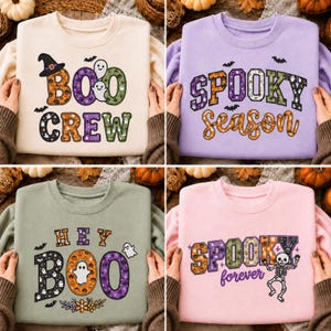 Op de afbeelding: Een collectie van vier sweaters met ronde hals in crème, lichtpaars, saliegroen en lichtroze. Elk is voorzien van Halloween-thema grafische prints met tekst waaronder BOO CREW, SPOOKY SEASON, HEY BOO en SPOOKY forever, versierd met spoken, vleermuizen en pompoenen.