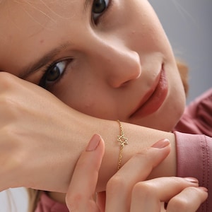 May include: A gold-colored bracelet featuring a Star of David charm. The delicate chain bracelet is worn on a wrist, with the charm centered. The bracelet is a simple, elegant piece of jewelry.