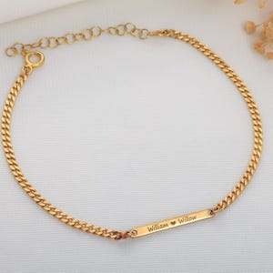May include: Gold-colored curb chain bracelet. A rectangular bar in the center is engraved with the names "William" and "Willow" separated by a heart symbol. The bracelet is displayed on a white surface.