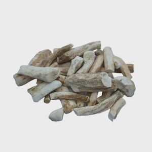 Könnte beinhalten: Ein Haufen getrockneter Wurzelstücke in hellbraunen und beigen Farbtönen. Die Stücke haben eine raue, strukturierte Oberfläche und unregelmäßige Formen. Der Hintergrund ist einfarbig hellgrau.