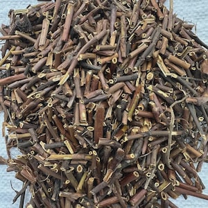May include: A close-up image of a pile of dried stems and twigs. The pieces are cut and vary in length and thickness, with shades of brown and tan. The cut ends and rough surfaces create a textured, natural appearance. The image shows the details of the plant material.