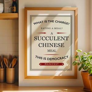 May include: A framed print with the text "WHAT IS THE CHARGE? EATING A MEAL? A SUCCULENT CHINESE MEAL THIS IS DEMOCRACY MANIFEST." The print is in a light wood frame, set against a neutral wall. Two potted plants sit on a wooden surface.