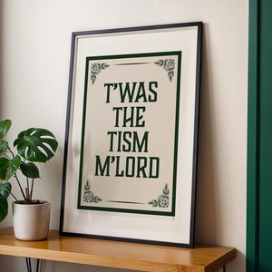 May include: A framed rectangular wall art print featuring a cream-coloured background with a dark green border and decorative floral corner accents. The text T'WAS THE TISM M'LORD is printed in a bold, dark green, serif-style capital font.