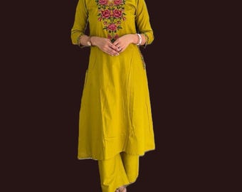 Puede incluir: Traje kurta bordado amarillo mostaza. El escote en V está adornado con bordados florales rosas y verdes. La kurta de manga tres cuartos se combina con pantalones palazzo a juego. El atuendo es de estilo indio tradicional.