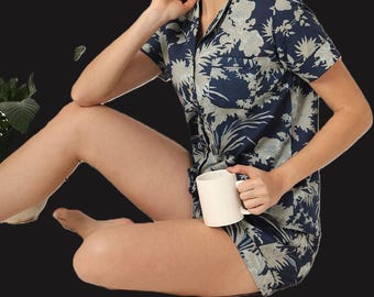 May include: Navy blue pajama set with a floral pattern in light blue and white. The set includes a short-sleeved button-down shirt and matching shorts. A white mug is held in the hand.