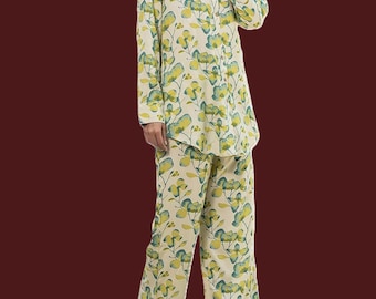 May include: A two-piece pajama set featuring a cream-colored background with a floral pattern in shades of yellow and teal. The set includes a button-down shirt and matching wide-leg pants. The pajamas are made of a soft, lightweight fabric.