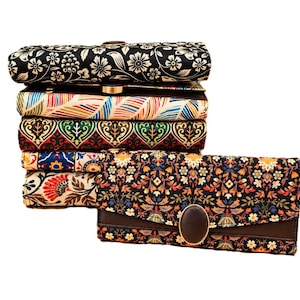May include: A stack of six rectangular wallets featuring various floral and geometric fabric patterns. Each wallet has a brown leather-like flap secured with a dark brown oval button closure. The patterns include black, white, blue, red, and green.