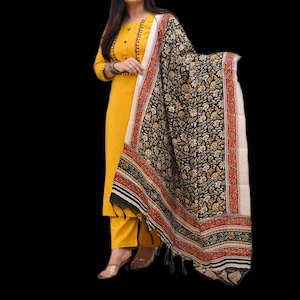 May include: A mustard yellow salwar kameez suit with a matching dupatta. The dupatta has a black floral pattern with red and cream borders. The outfit features detailed embroidery around the neckline and sleeves.