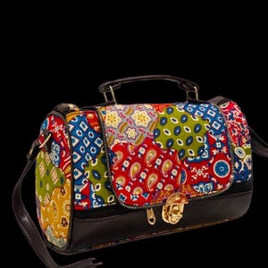 Puede incluir: Bolso bandolera patchwork colorido con base y asa negras. El bolso presenta una variedad de patrones en rojo, azul, verde y amarillo. Tiene un cierre y cremallera dorados.