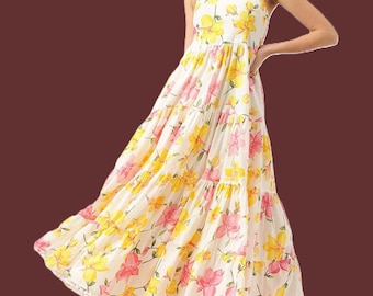 May include: A floor-length white sleeveless dress featuring a tiered skirt and a vibrant floral pattern in shades of yellow and pink. The garment has a square neckline with thick straps and a delicate white pom-pom trim along the bottom hemline.