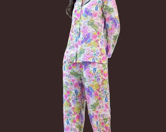 Può includere: Un set pigiama a due pezzi composto da una camicia a maniche lunghe con bottoni e colletto a revers e pantaloni lunghi abbinati. Il set è realizzato in tessuto bianco con una vivace stampa floreale multicolore nei toni del rosa, viola e verde.