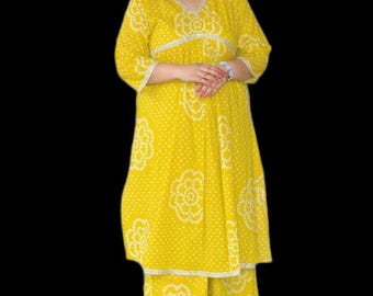 Könnte beinhalten: Ein leuchtend gelbes Tunika- und Hosen-Set mit weitem Bein, verziert mit einem weißen Punktemuster und großen kreisförmigen Blumenmotiven. Die Tunika hat einen V-Ausschnitt, Dreiviertelärmel und eine geraffte Taille mit silberfarbener Borte.