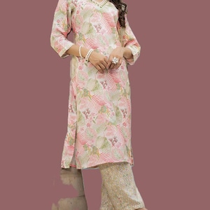 May include: A two-piece floral print outfit in pink, white, and green. The top has a V-neck and three-quarter sleeves. The trousers are a light yellow with a subtle pattern. The outfit is accessorized with a white scarf and bracelets.