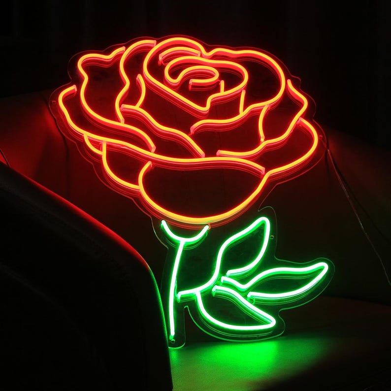 Pu&ograve; includere: Un'insegna al neon a forma di rosa. La rosa &egrave; delineata in rosso e arancione, con foglie e stelo verdi. L'insegna &egrave; illuminata su uno sfondo scuro.